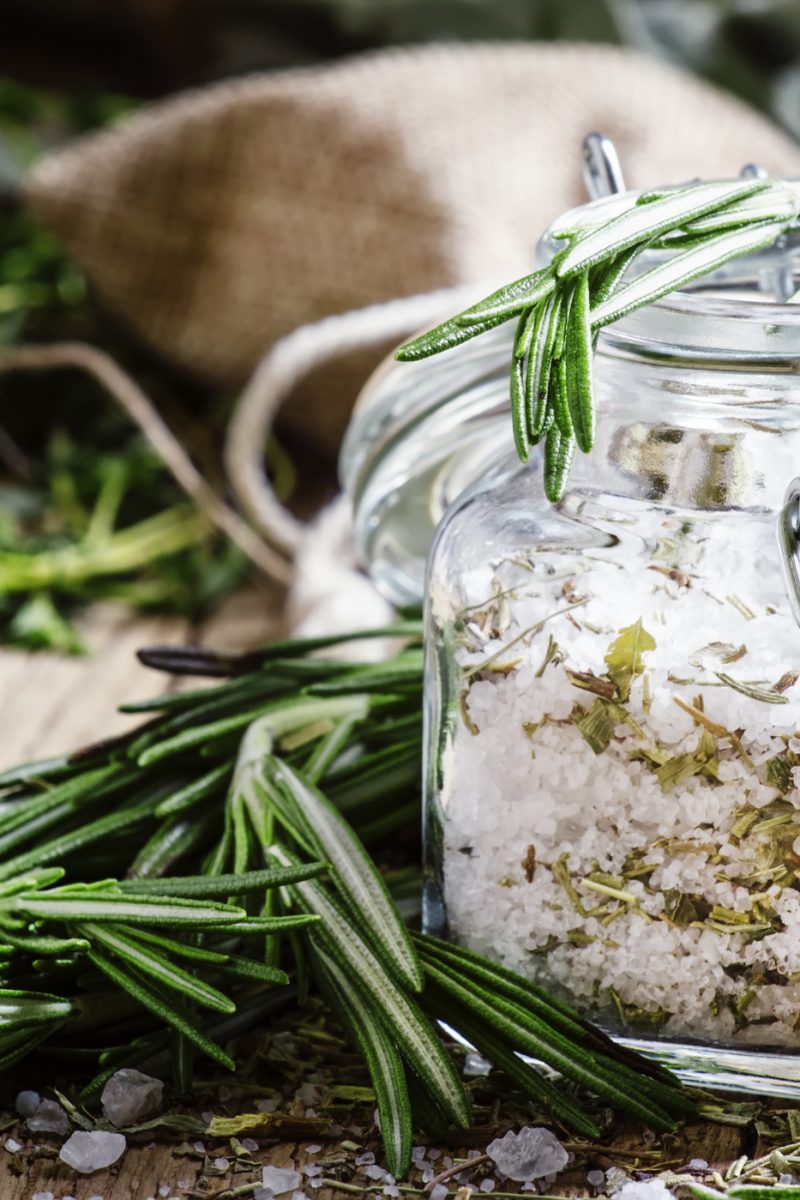 Sea salt with dried rosemary in a glass jar, vintage wooden background, selective focus